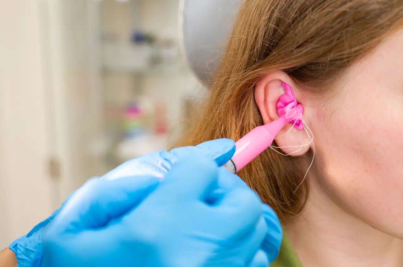 An audiologist taking an ear impression with bright pink moulding material