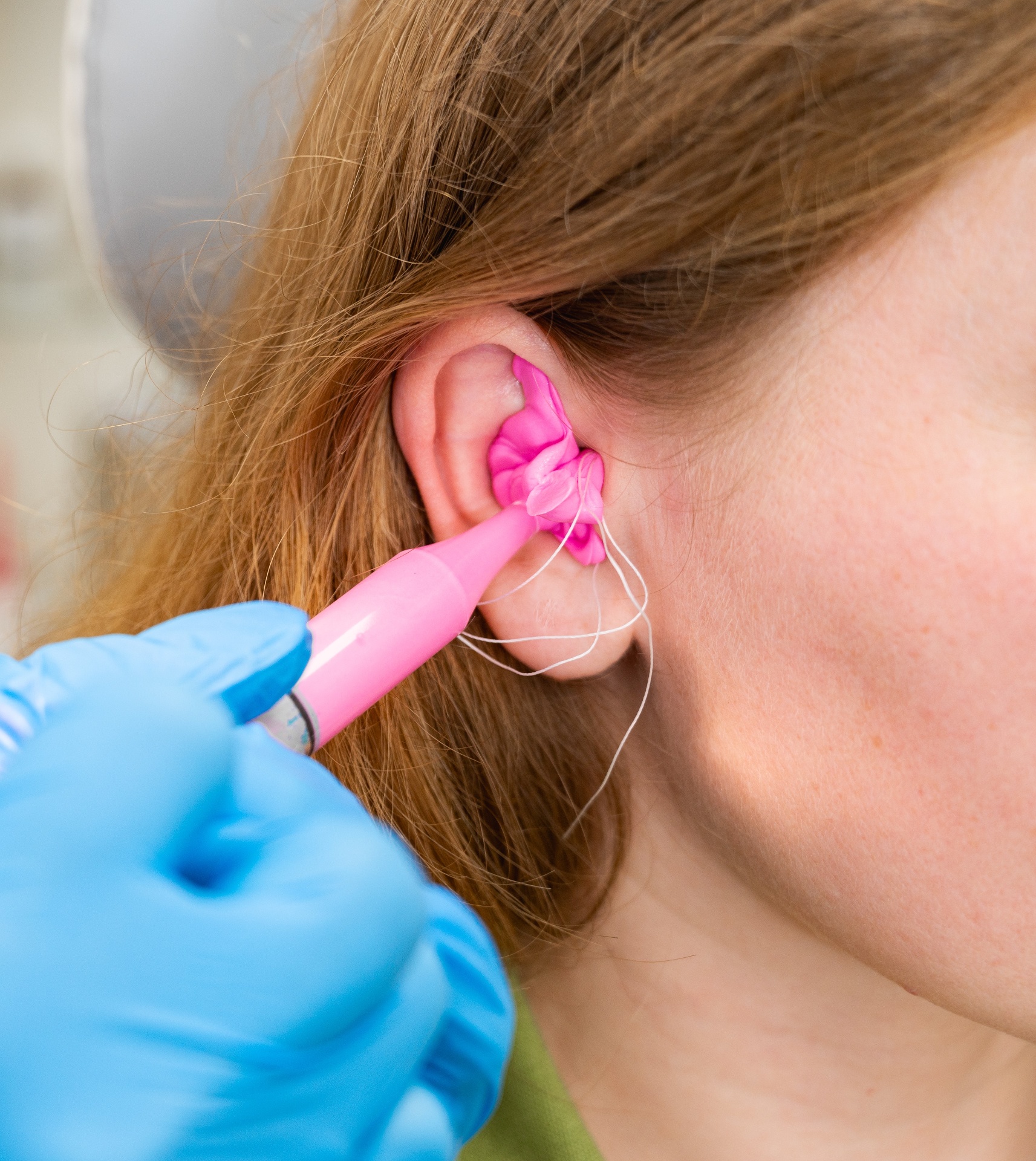 An audiologist taking an ear impression with bright pink moulding material