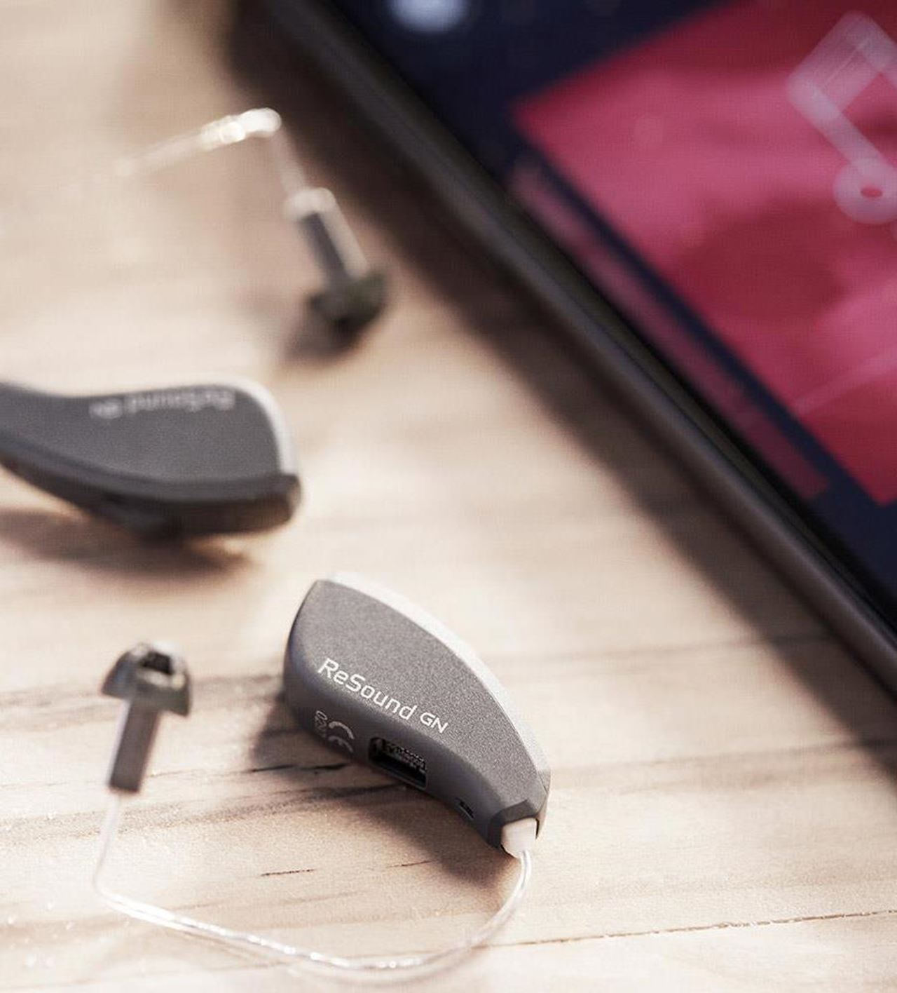 A small rechargeable hearing aid resting in its charging case, fitted at our Kenfig Hill, Bridgend clinic